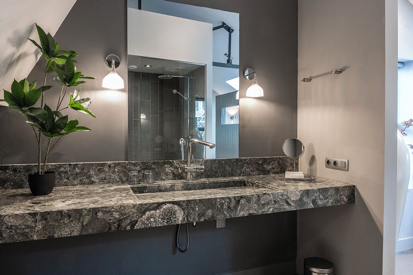 A bathroom with a granite countertop, a modern sink, a mirror, and a potted plant.
