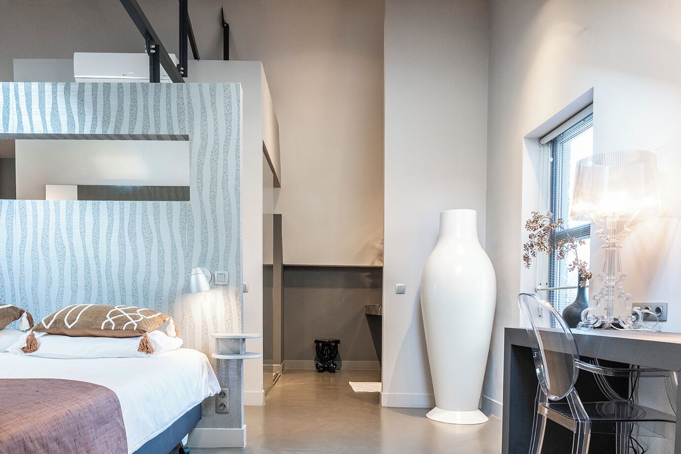 A modern bedroom with a bed, bedside table, and a large white vase.