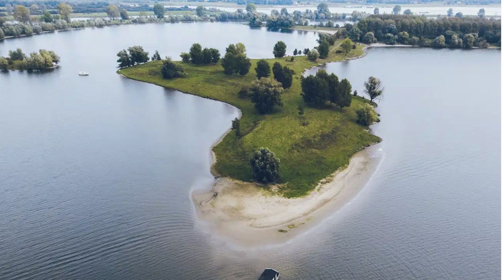An aerial view of a lakeside property with a sandy beach, grassy areas, and scattered trees.