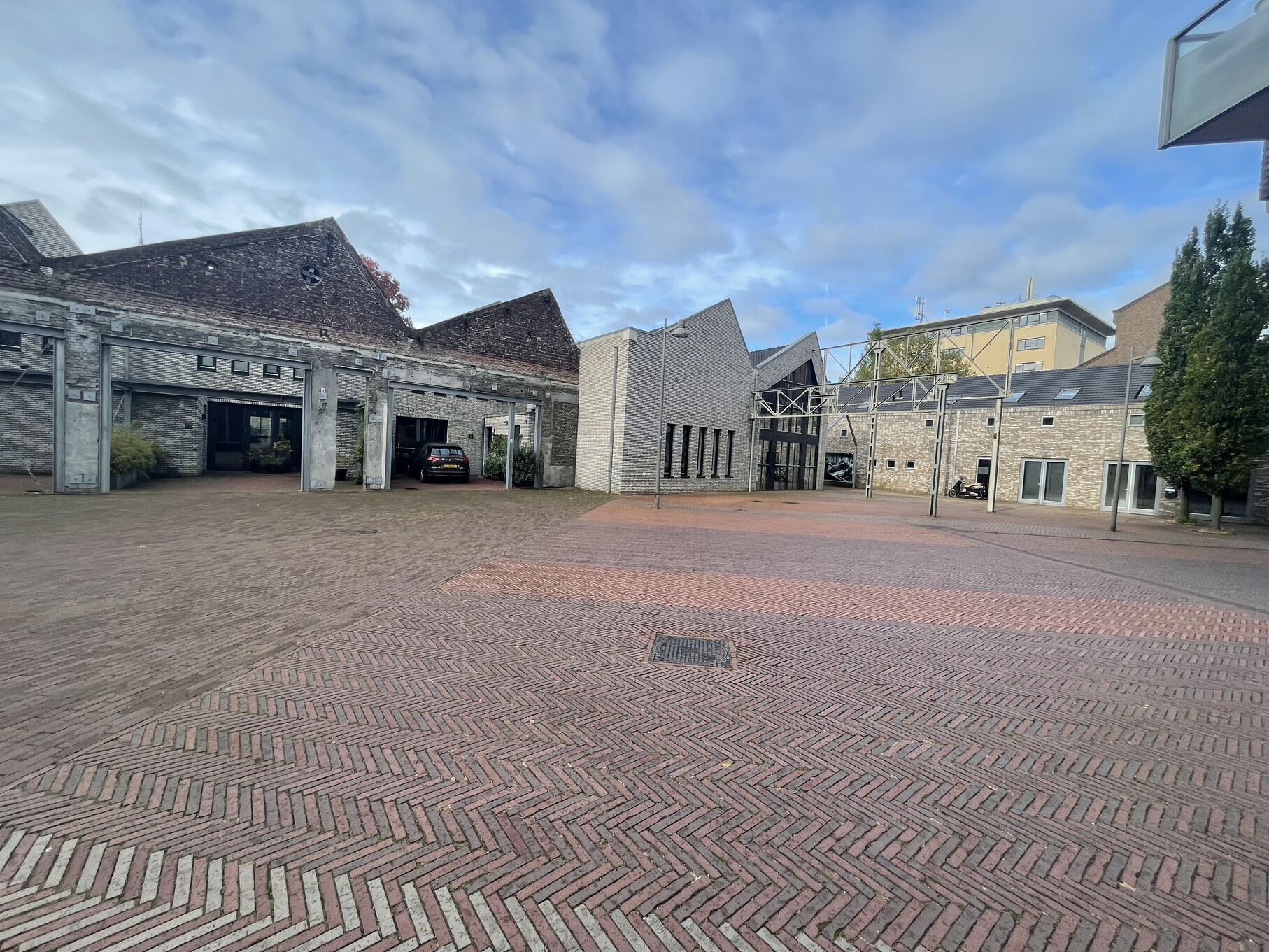 A spacious courtyard with a brick-patterned floor, surrounded by modern buildings with large windows and a mix of brick and stone facades.