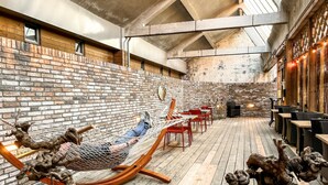 A cozy outdoor seating area with a hammock, wooden tables, and chairs, surrounded by a brick wall and wooden beams. - Cozy and stylish room near Oss highlights, with free parking and fast WiFi for a comfortable and convenient stay. (Oss)