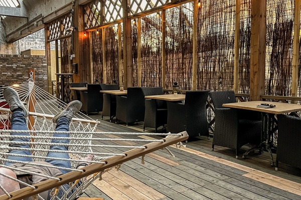 Cozy wooden terrace with lounge chairs, wicker dining tables, warm lighting, and natural bamboo screens creating a relaxed outdoor atmosphere.