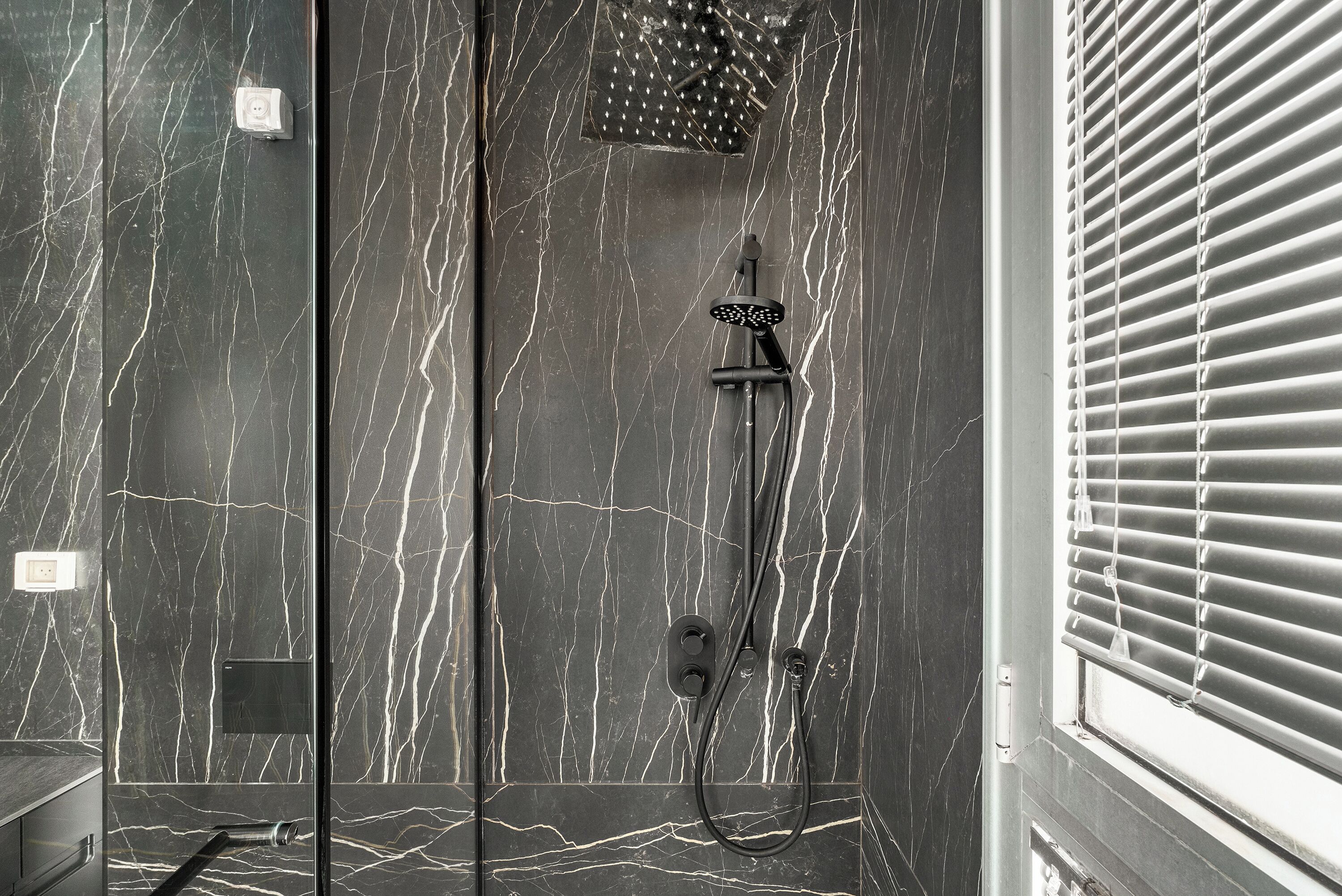 Une salle de bain moderne avec une douche, des murs en marbre et une fenêtre avec des stores.