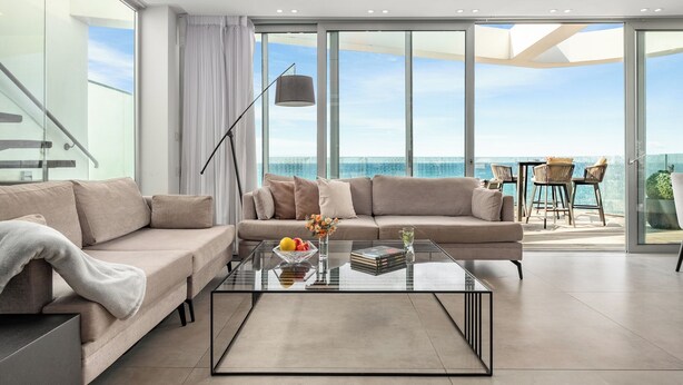 A modern living room with a glass coffee table, beige sofa, and a view of the ocean through large windows. - Rooftop Jacuzzi Penthouse by Sea N' Rent (Haifa)