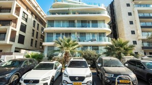 A modern multi-story building with balconies, parked cars, and palm trees. - Rooftop Jacuzzi Penthouse by Sea N' Rent (Haifa)