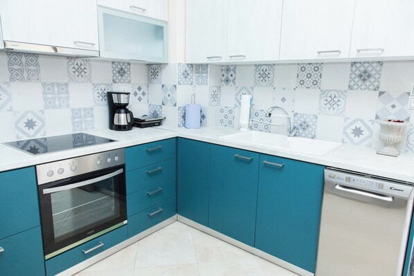 A kitchen with teal cabinets, a white countertop, a coffee maker, an oven, and a dishwasher. - Great Apartment in Piraeus (Piraeus)