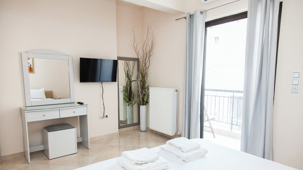 Una habitación de hotel moderna con cama, escritorio, televisor y balcón con cortinas.