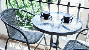 Un balcón con dos sillones de mimbre y una pequeña mesa redonda con dos tazas negras.