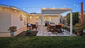 A backyard patio with a covered dining area, outdoor kitchen, and string lights.