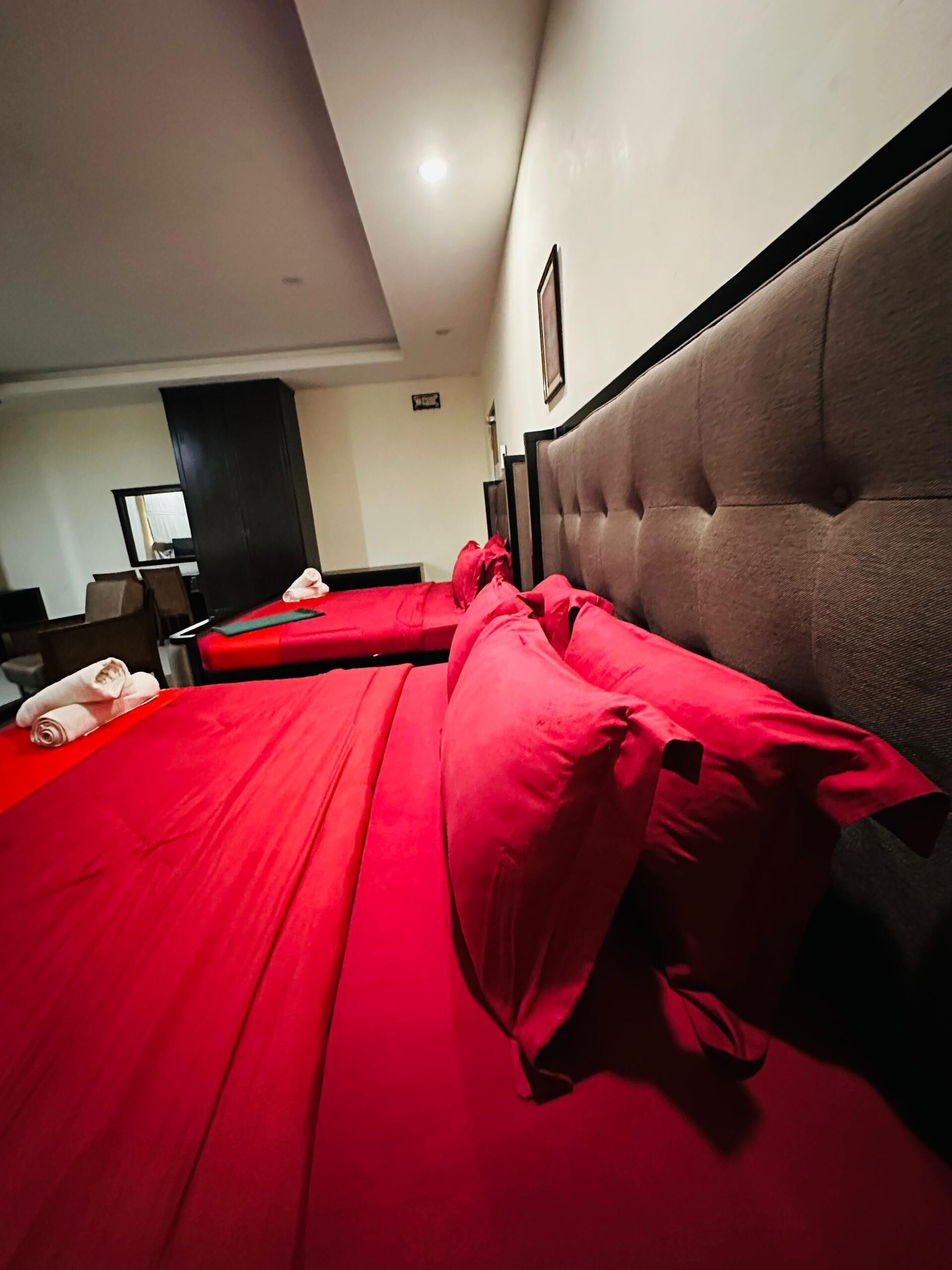A hotel room with two beds, each with red bedding and a tufted headboard.