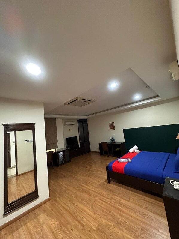 A hotel room with a bed, a desk, a chair, a television, and a mirror.