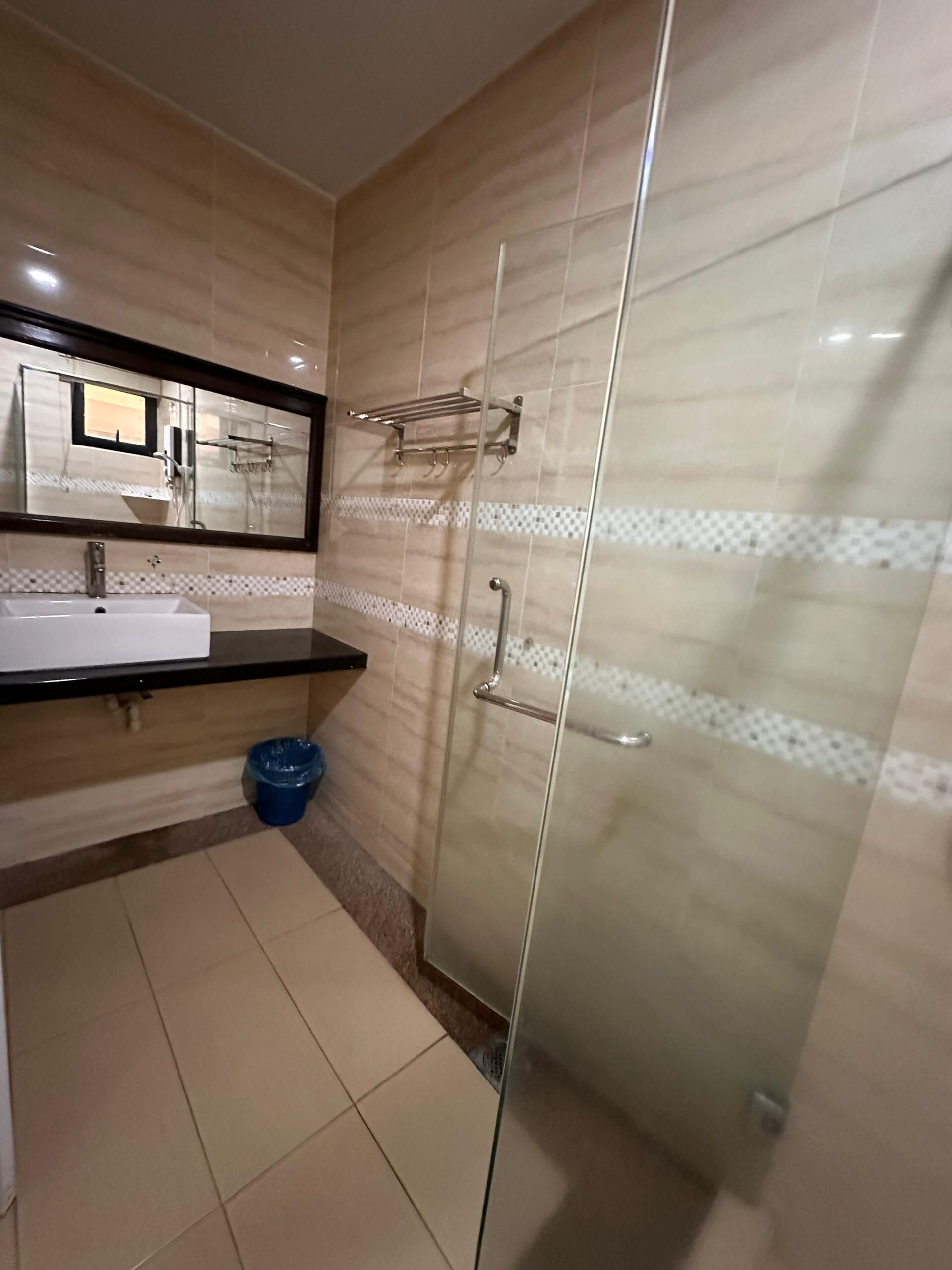 Un baño moderno con cabina de ducha de vidrio, un lavabo con espejo y un cubo de basura azul.