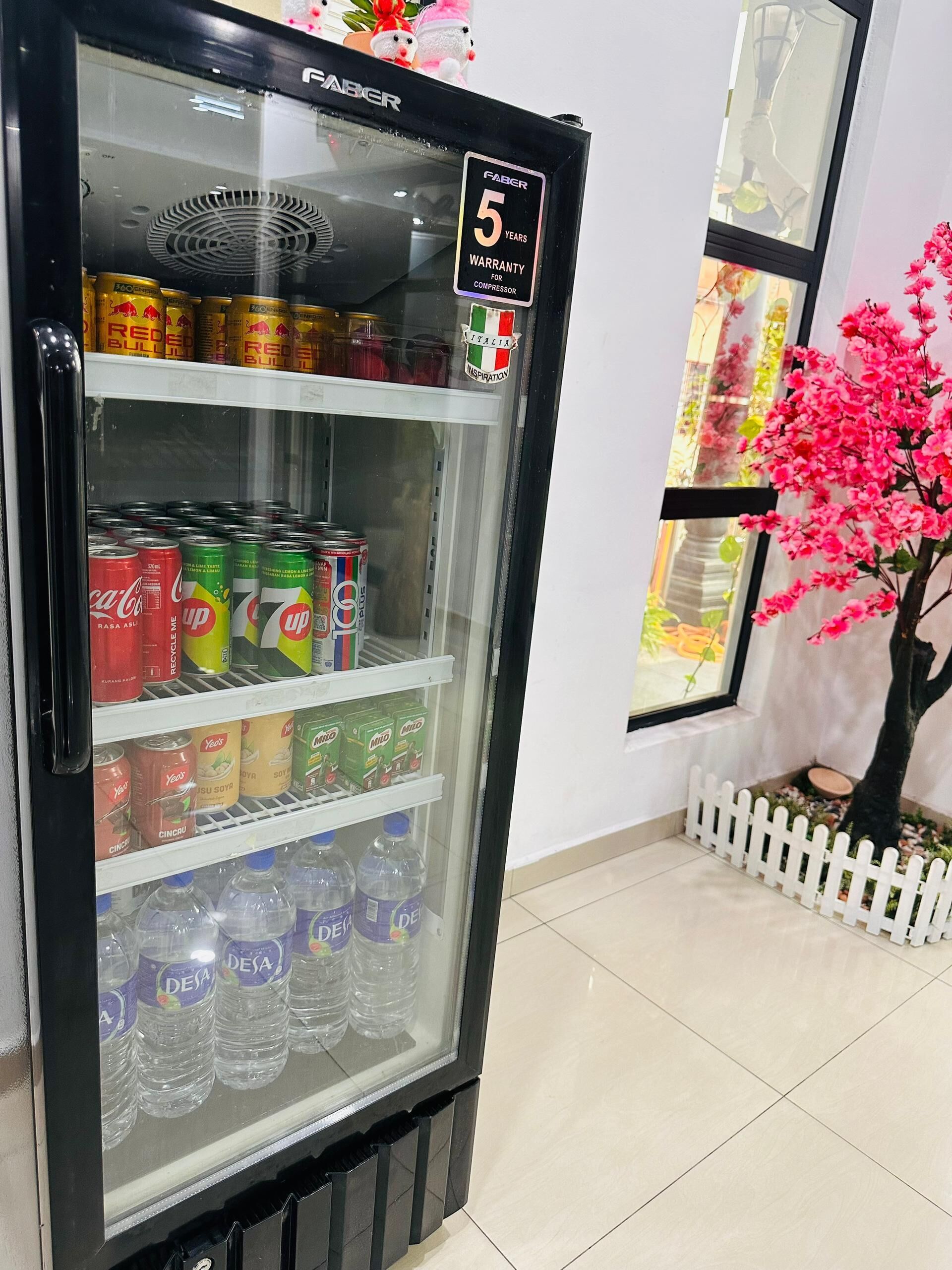 Jääkaappi, joka on täynnä erilaisia juomia, kuten Coca-Colaa, 7UP:ia ja Nesteaa, ja jossa on kyltti, jossa kerrotaan, että sillä on 5 vuoden takuu.