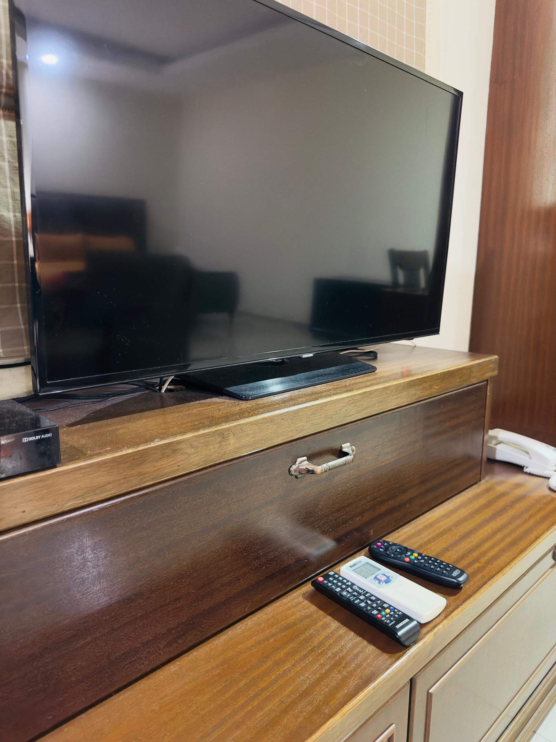 Een houten tv-meubel met een flatscreen televisie, een afstandsbediening en een telefoon.