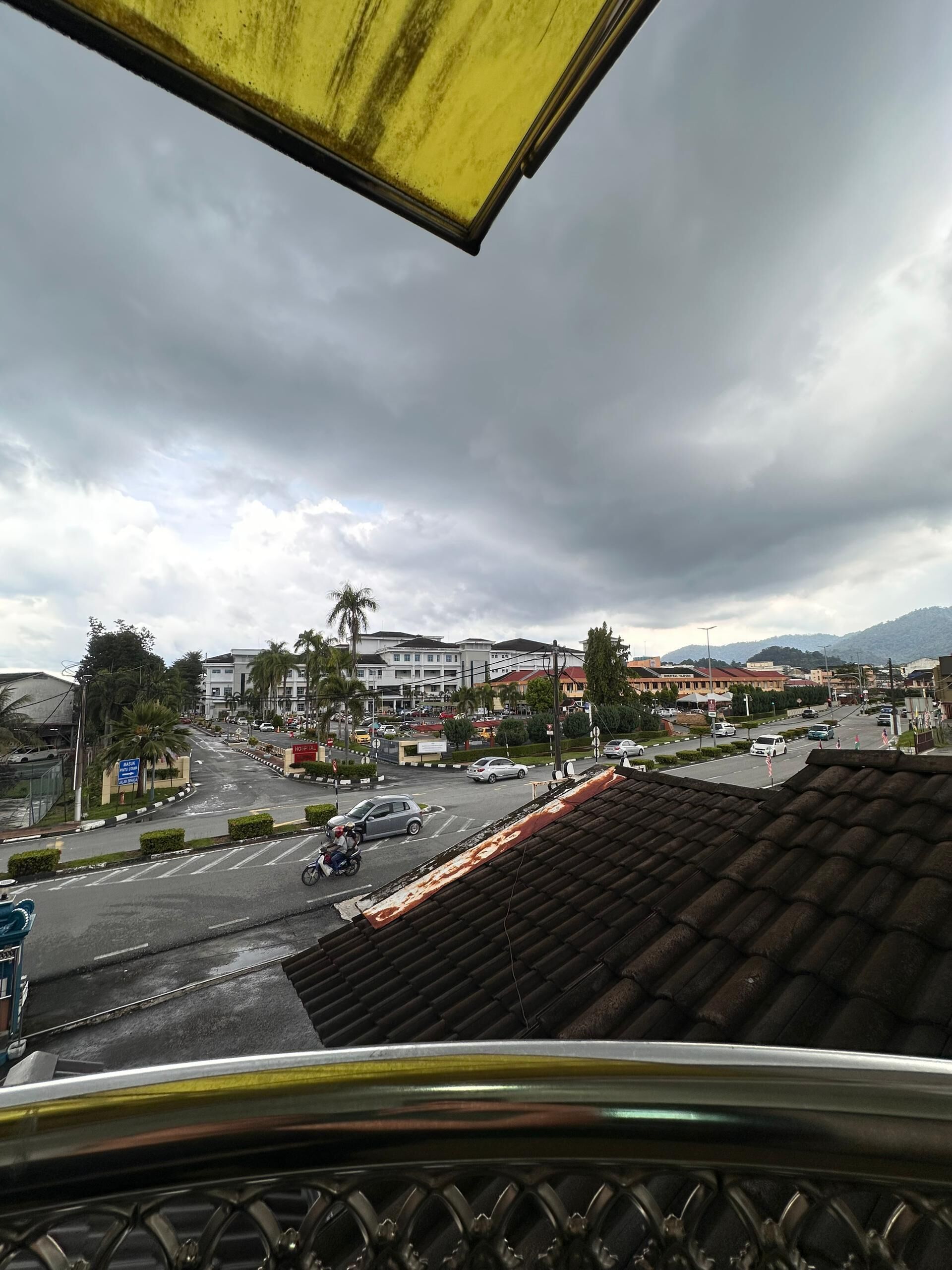 Vista desde un balcón sobre una calle de la ciudad con edificios, palmeras y un cielo nublado.