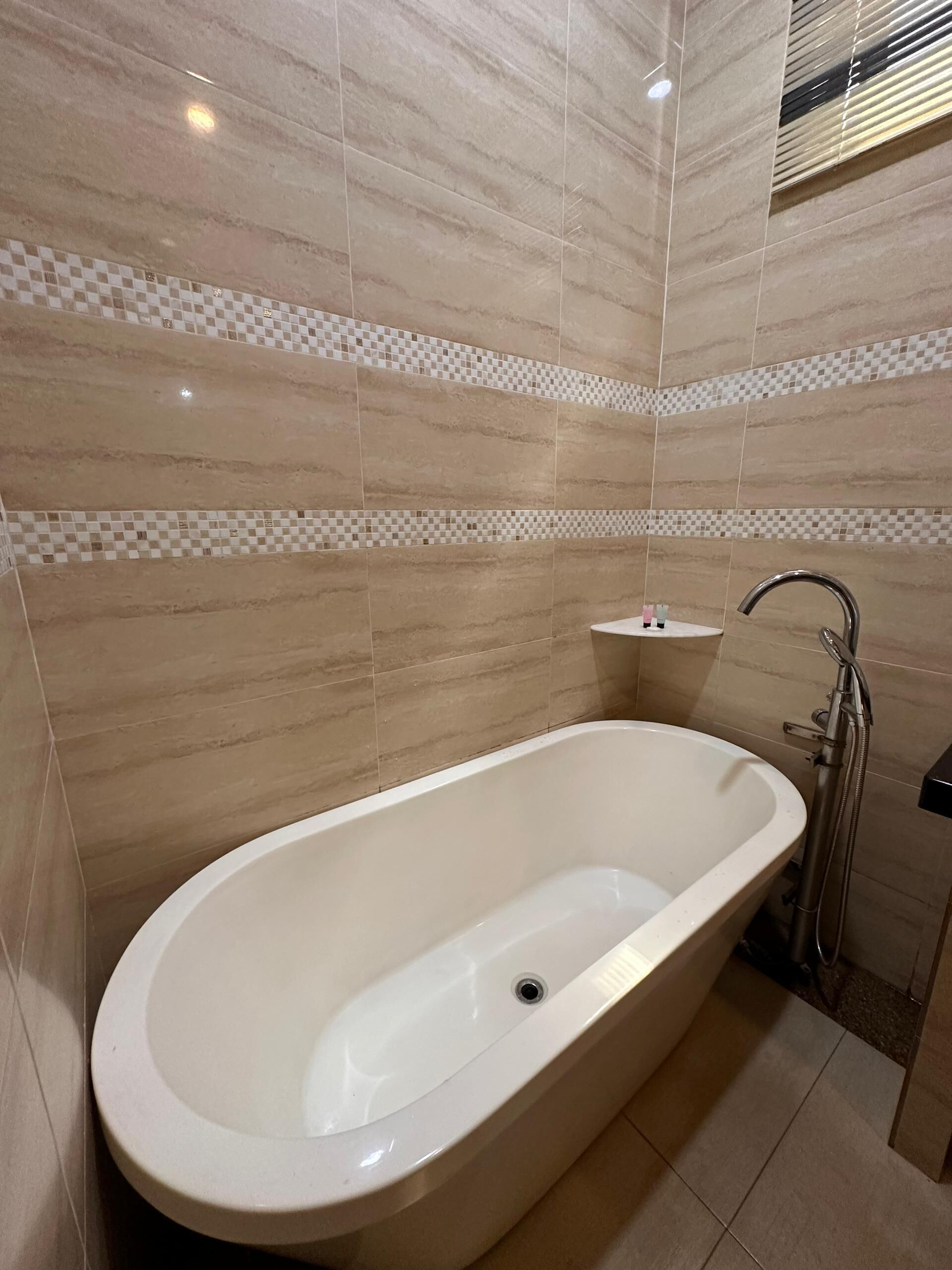 Un baño moderno con una bañera independiente, paredes con azulejos y un pequeño estante con artículos de aseo.