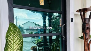 Entrada de hotel con un cartel de 'WELCOME', un cartel de 'VISA' y un cartel de 'MAXWELL INN'.