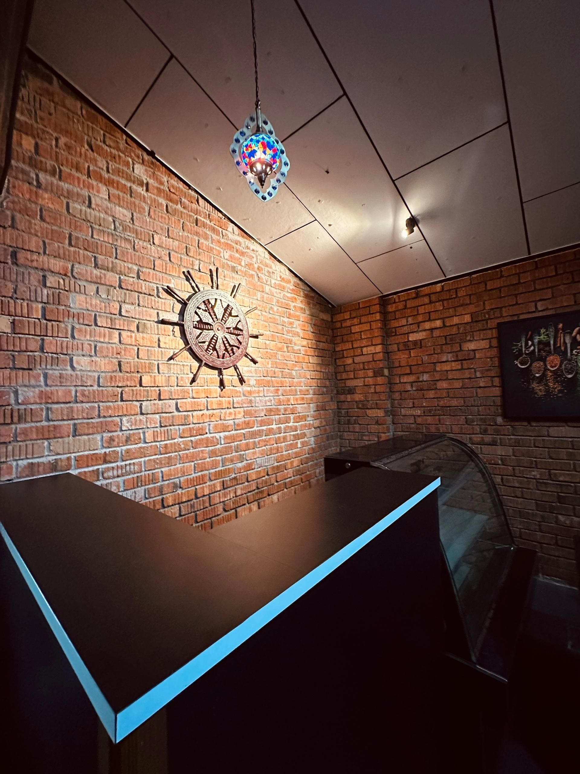 Interior de restaurante con pared de ladrillo, un reloj decorativo y una lámpara colgante.