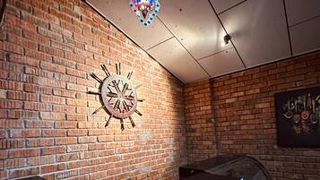 Interior de restaurante con pared de ladrillo, un reloj decorativo y una lámpara colgante.
