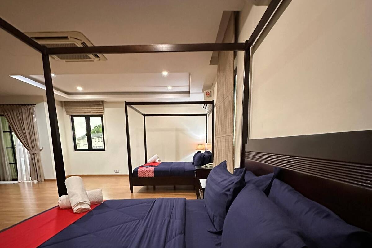 Une chambre d’hôtel moderne avec un grand lit, un lit plus petit et un canapé. On y trouve une fenêtre avec des rideaux, une table de chevet et une lampe.