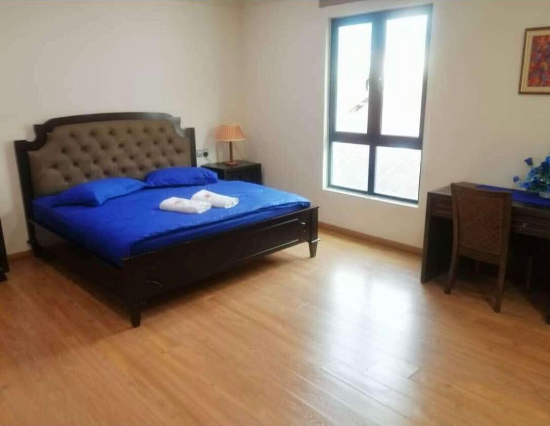 A bedroom with a bed, a desk, a chair, a window, and a lamp.