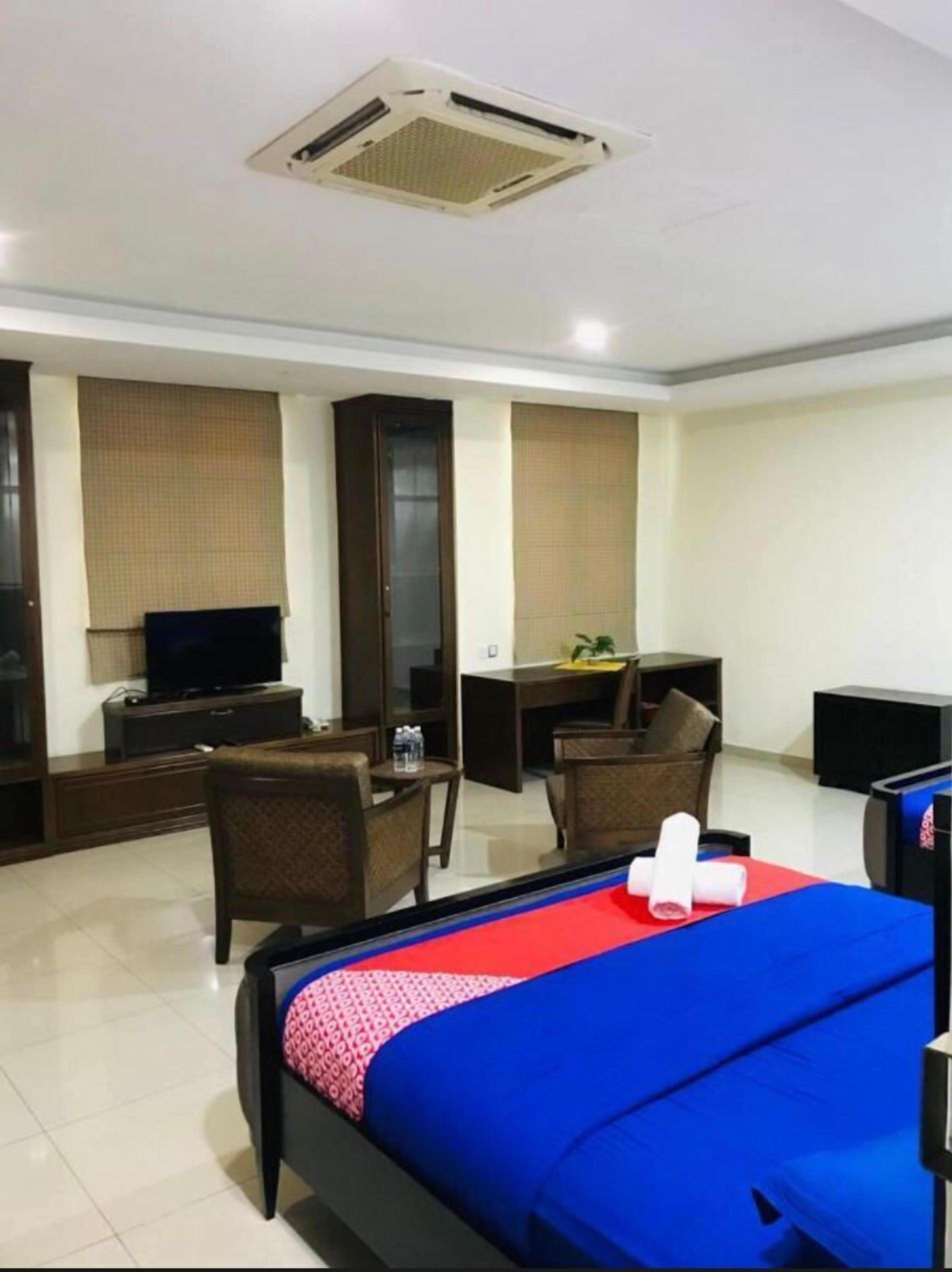 A hotel room with a bed, a desk, a chair, a television, and a minibar.