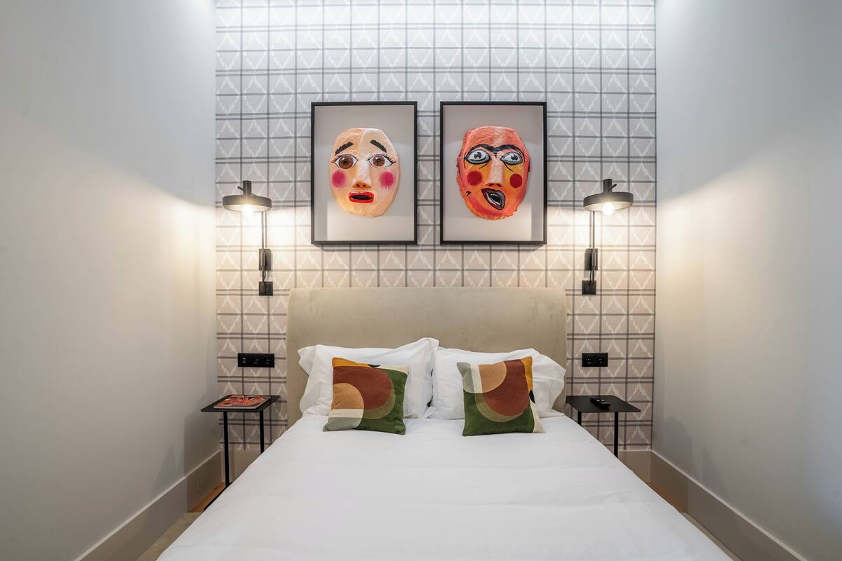 Ein Hotelzimmer mit einem Bett, zwei gerahmten Bildern an der Wand, einem Kopfteil und zwei Nachttischen mit Lampen.