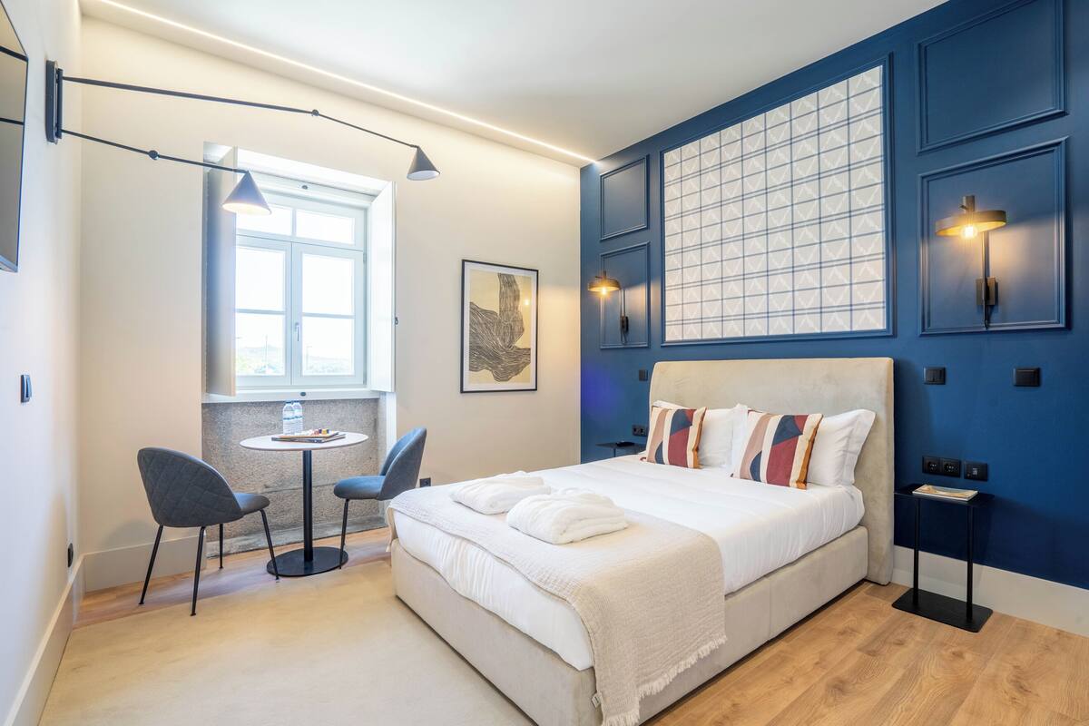 Ein modernes Schlafzimmer mit einem großen Bett, einem kleinen Tisch mit Stühlen und einem Fenster, das für natürliches Licht sorgt.