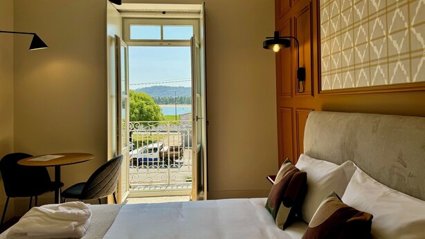 Une chambre d’hôtel comprenant un lit, une table, une chaise et un balcon avec vue sur un lac et des montagnes.