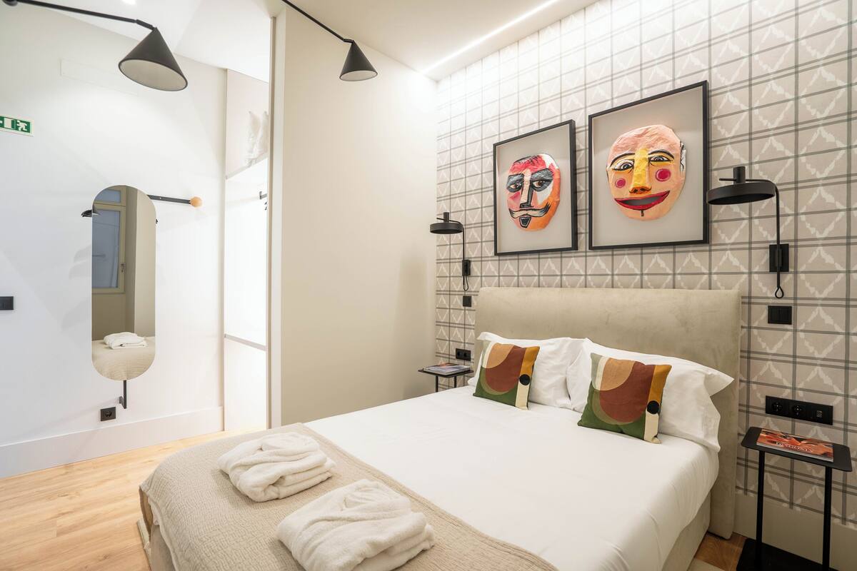 Ein modernes Hotelzimmer mit einem großen Bett, zwei Wandlampen und zwei gerahmten Kunstwerken darüber.