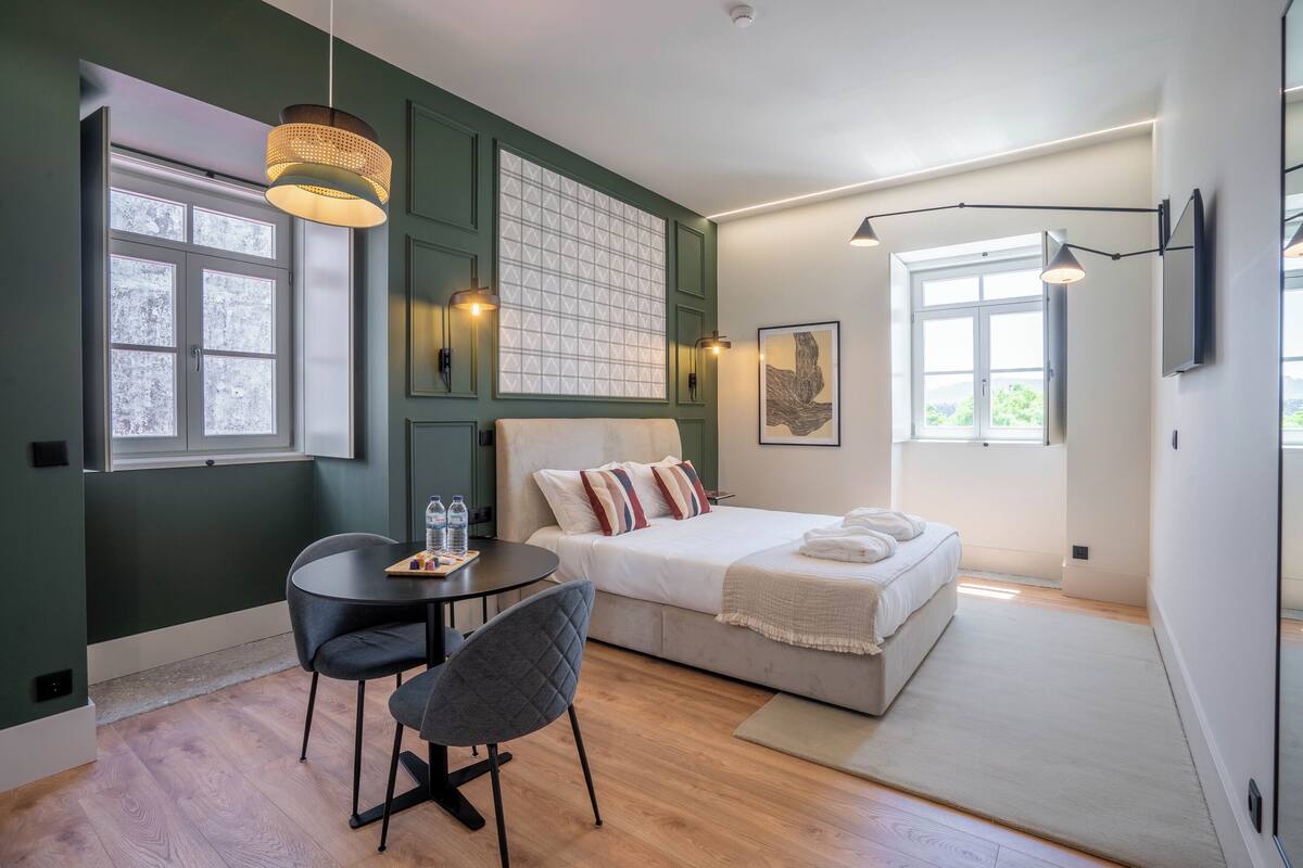 Ein modernes Schlafzimmer mit Bett, Schreibtisch und Stuhl, mit einem großen Fenster und Blick ins Freie.