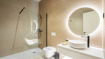 Un baño moderno con cabina de ducha de vidrio, espejo redondo, lavamanos blanco y un inodoro.