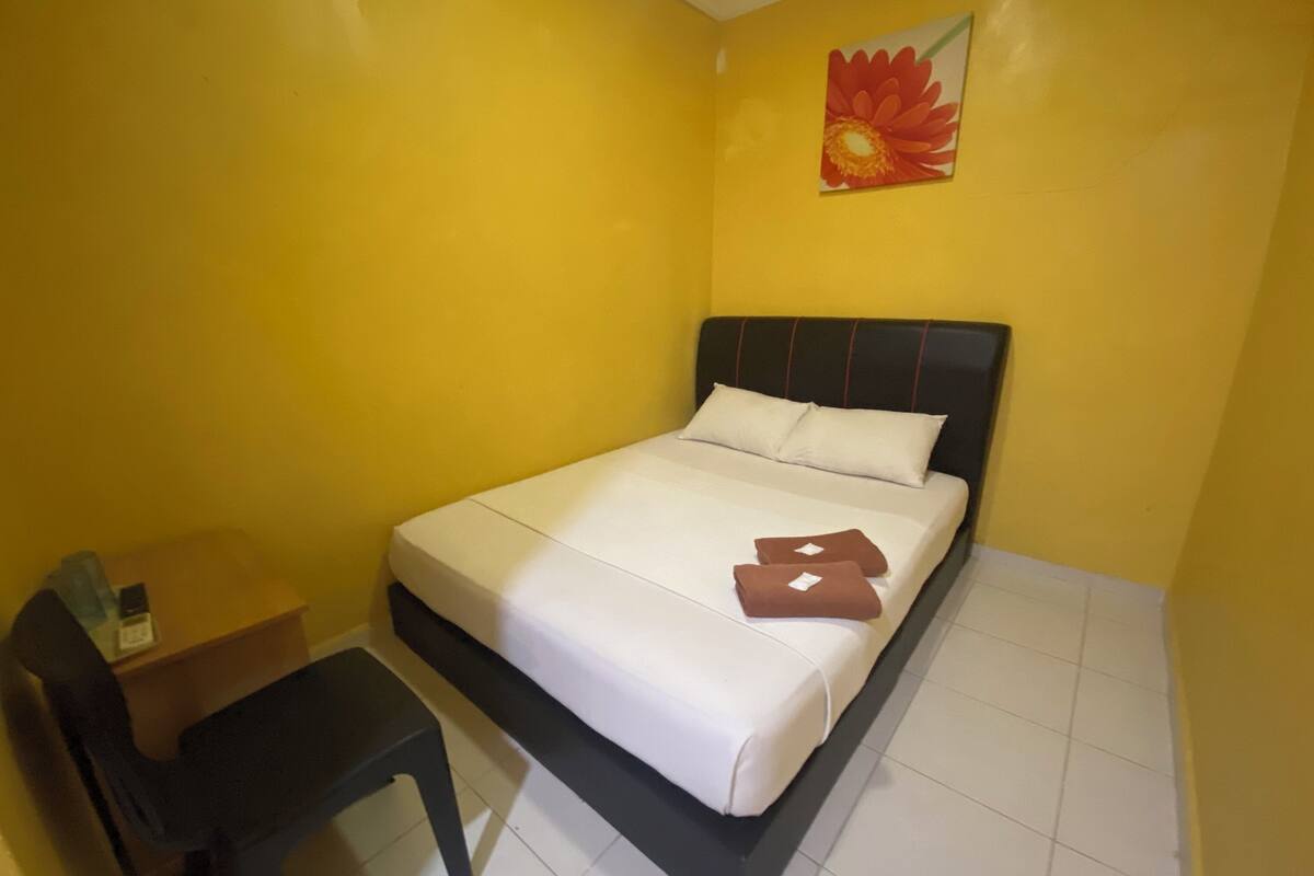 Un dormitorio pequeño con paredes amarillas, una cama individual, un escritorio y una silla.