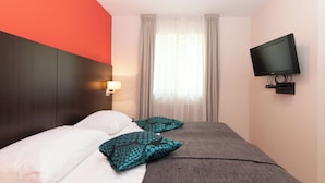 Une chambre d’hôtel avec un lit, des oreillers, une télévision et une fenêtre avec des rideaux.
