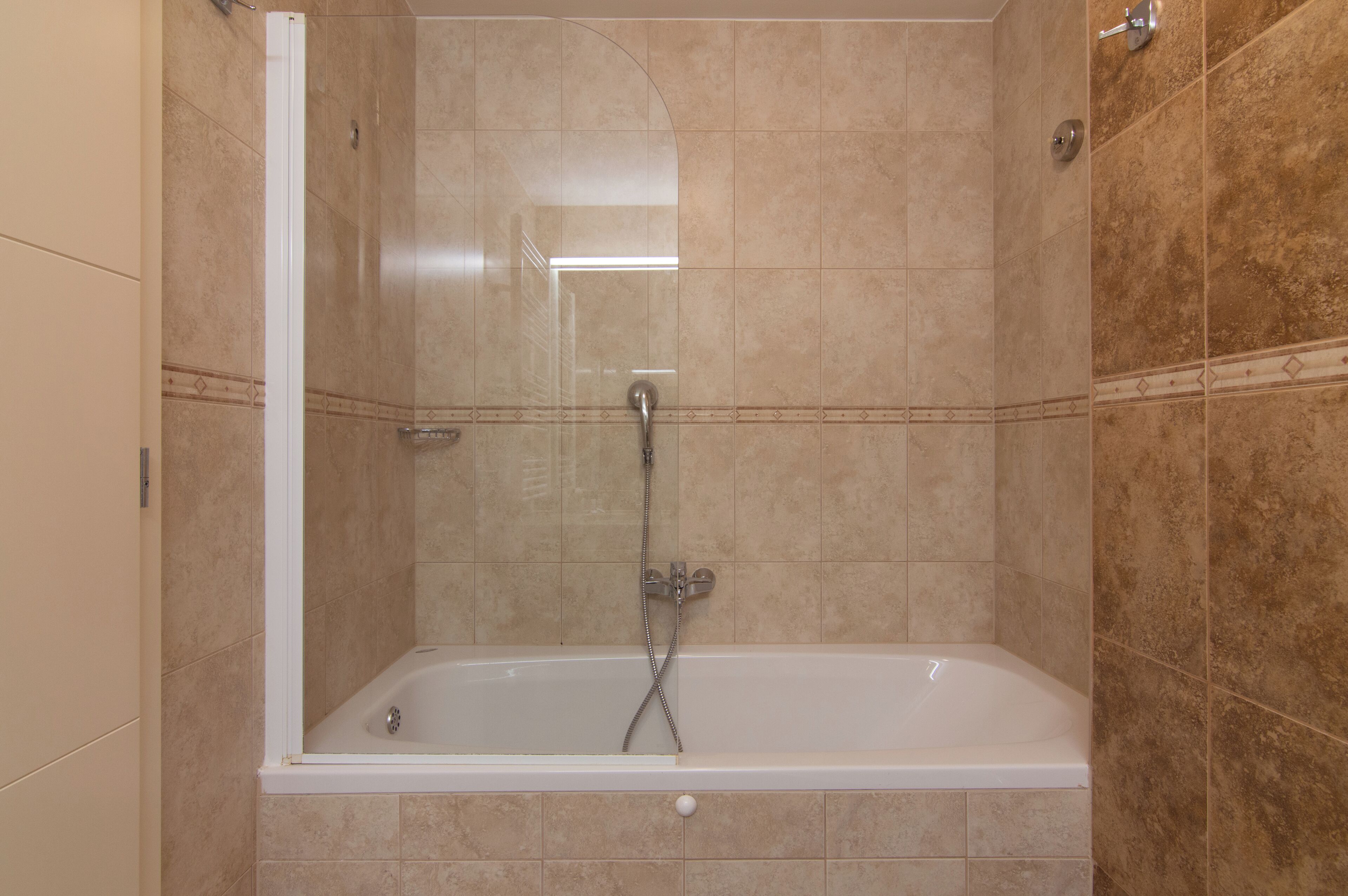 A walk-in shower with a glass door, a bathtub, and tiled walls.