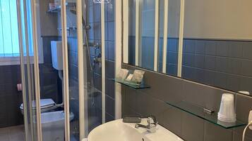 A bathroom with a glass shower enclosure, a white sink with a mirror above it, and a glass shelf with toiletries.