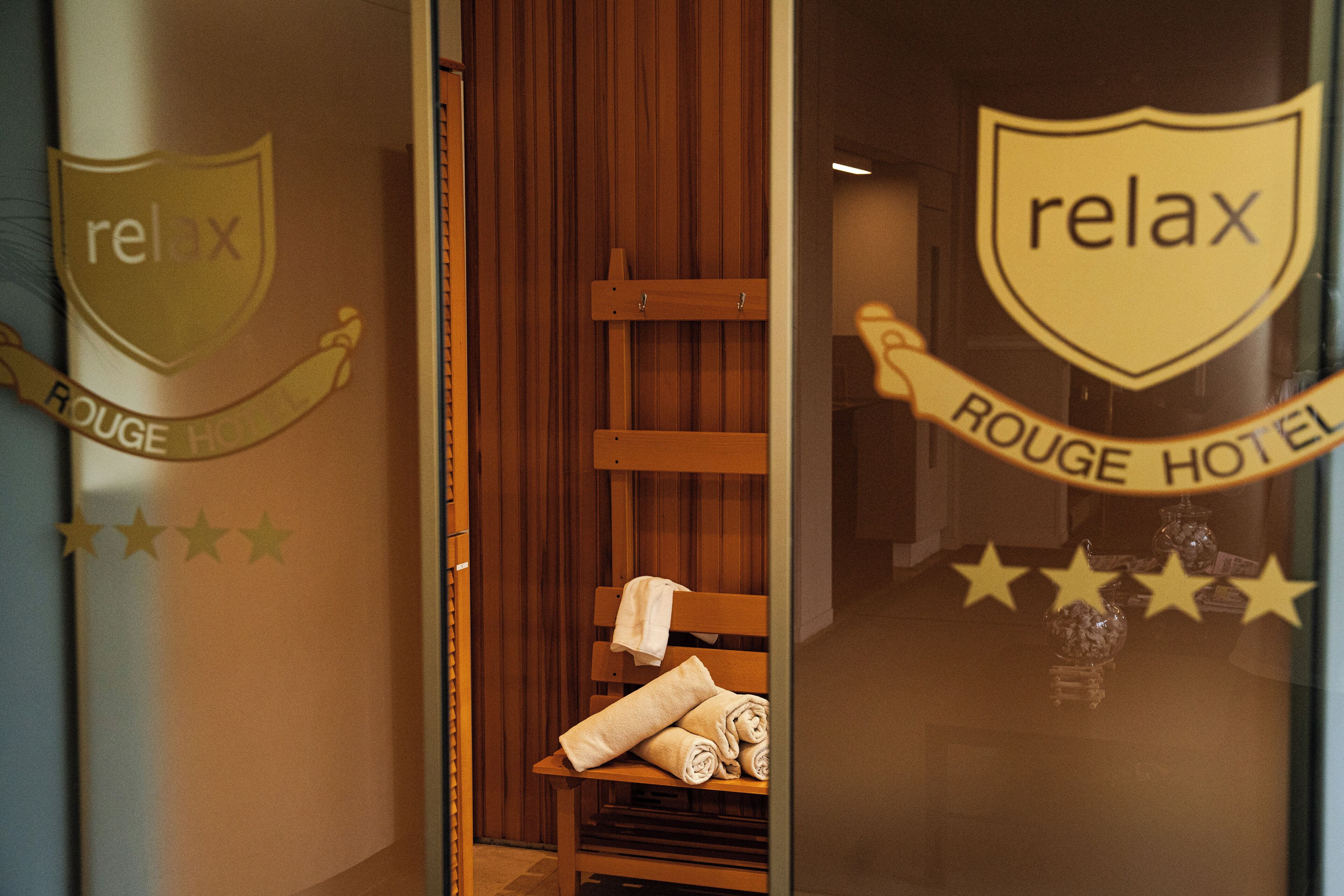 Habitación de hotel con un banco de madera, toallas y un cartel que dice 'Relax'.