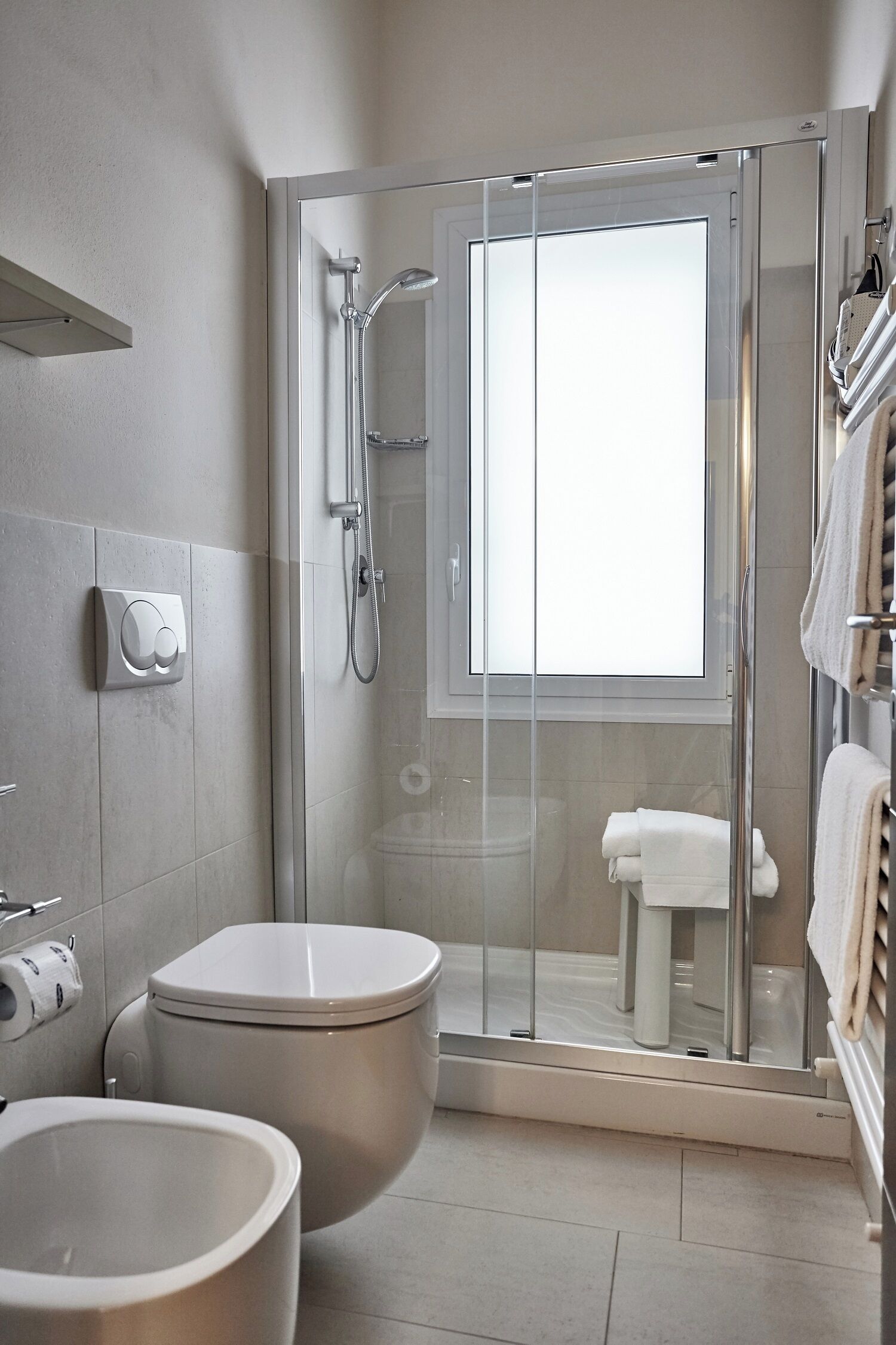 A modern bathroom with a glass-enclosed shower, a toilet, and a bidet.