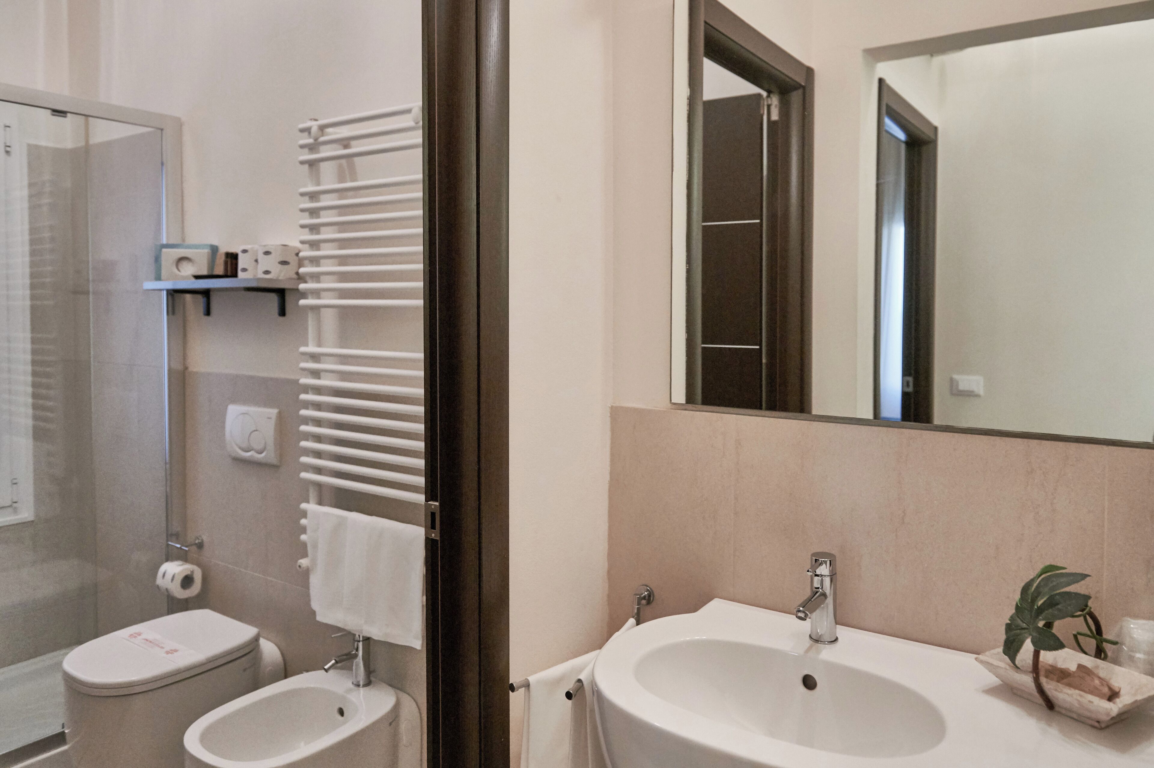 Une salle de bain équipée d’une douche, de toilettes, d’un bidet, d’un lavabo et d’un grand miroir.