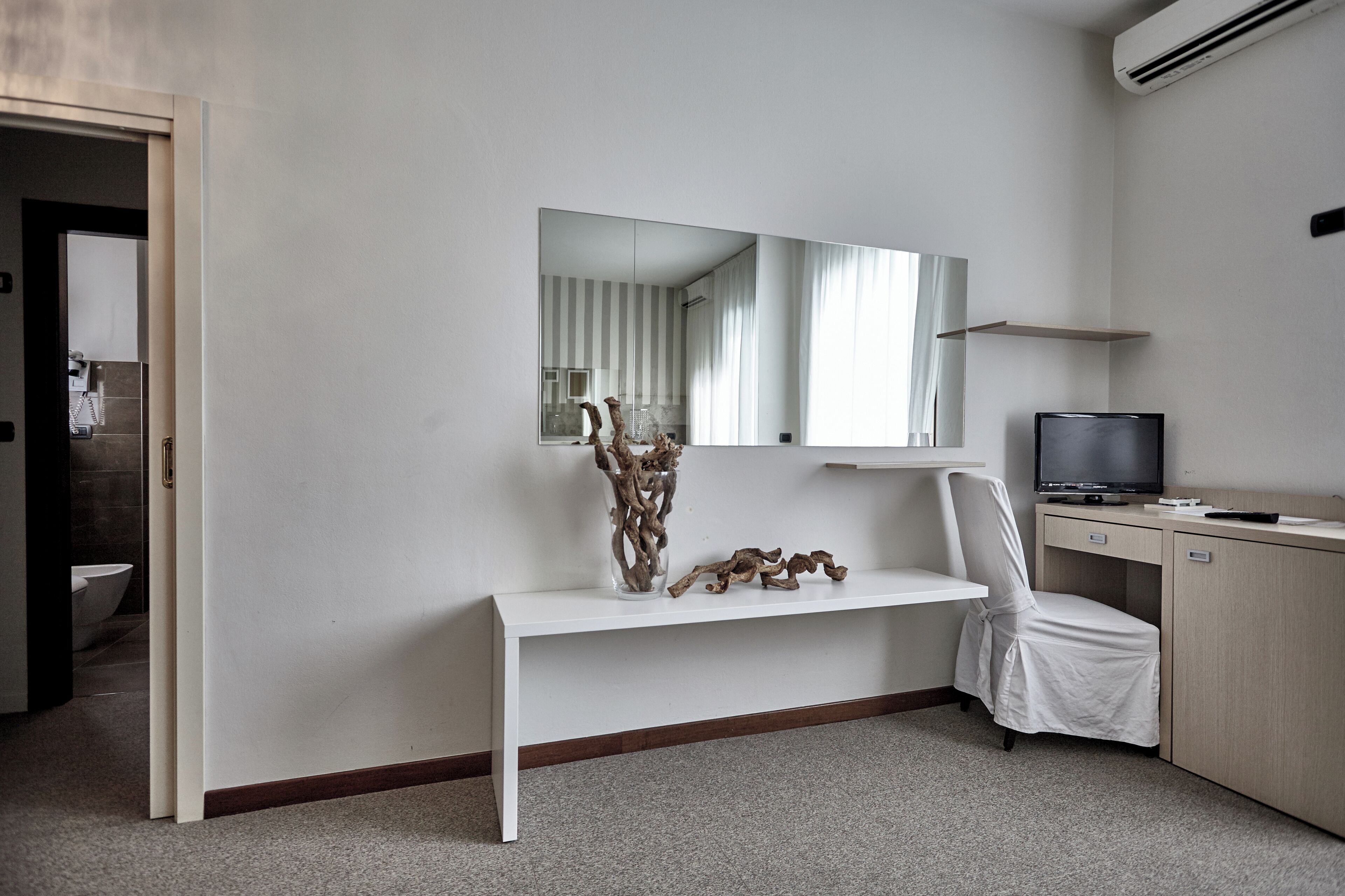 Una habitación de hotel moderna con una mesa consola blanca, un espejo, un televisor y un escritorio.