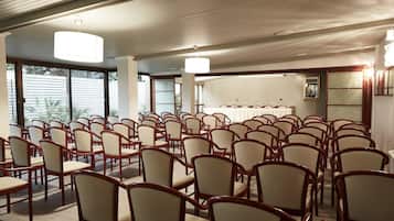 Une salle de conférence avec des rangées de chaises beiges, de grandes fenêtres et un plafond en bois.