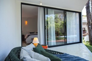 Relax in a comfortable seating area with a woven basket and cushions, surrounded by lush greenery through a large sliding glass door.