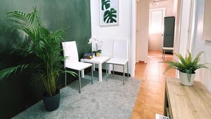 A hallway with a grey carpet, white chairs, a small table, and potted plants.