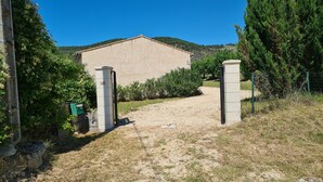 Un carrer de grava que condueix a un edifici de façana beig, envoltat de vegetació i un cel blau clar.