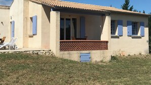 Una casa de planta baixa amb teulada de rajola, un porxo amb barana de celosies i una porta blava petita.