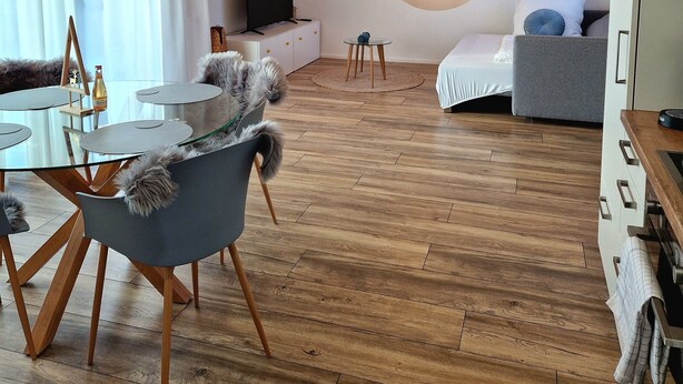 A modern room with a wooden ceiling, a round wall-mounted TV, a dining table with chairs, and a sofa.