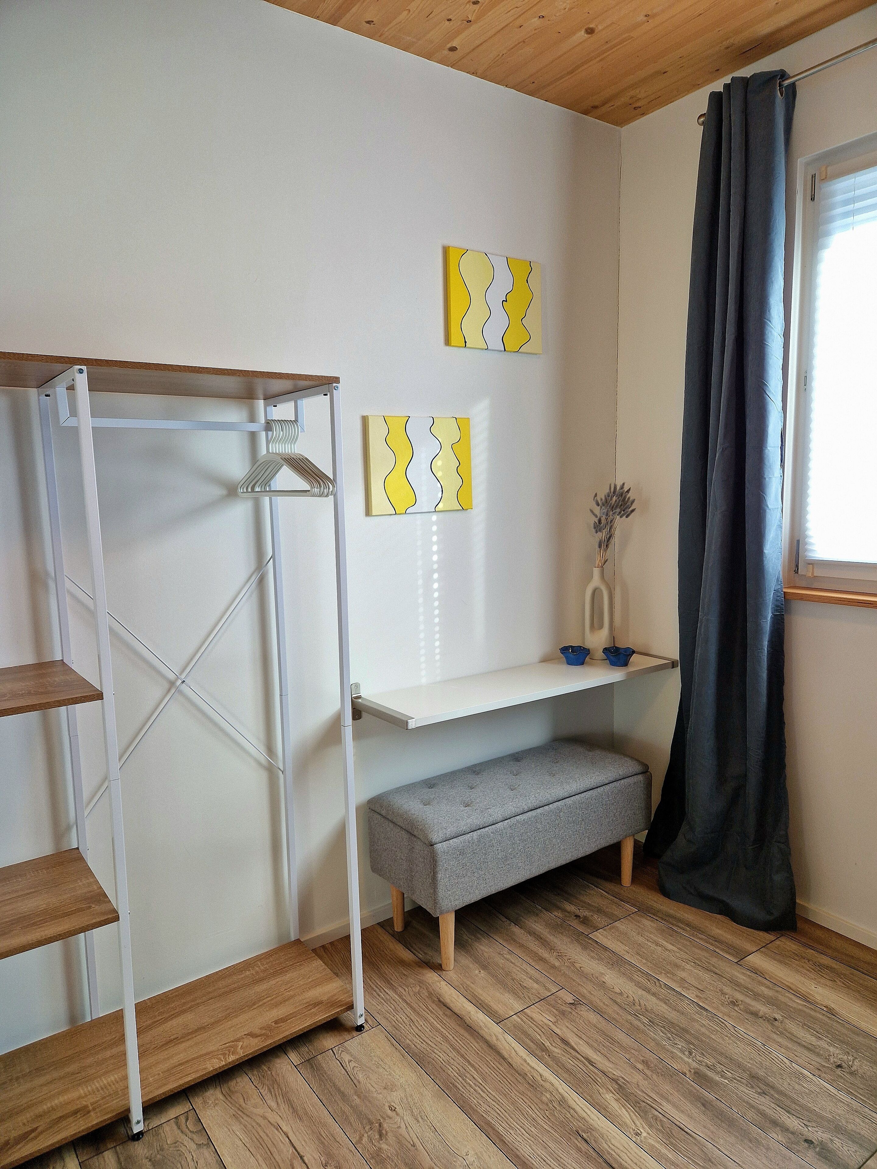 Een kamer met een wit metalen wandrek, een grijze bank, houten vloeren en twee gele en witte kunstwerken aan de muur.
