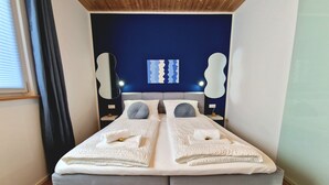 A modern bedroom with a grey bed, white linens, and a blue accent wall.