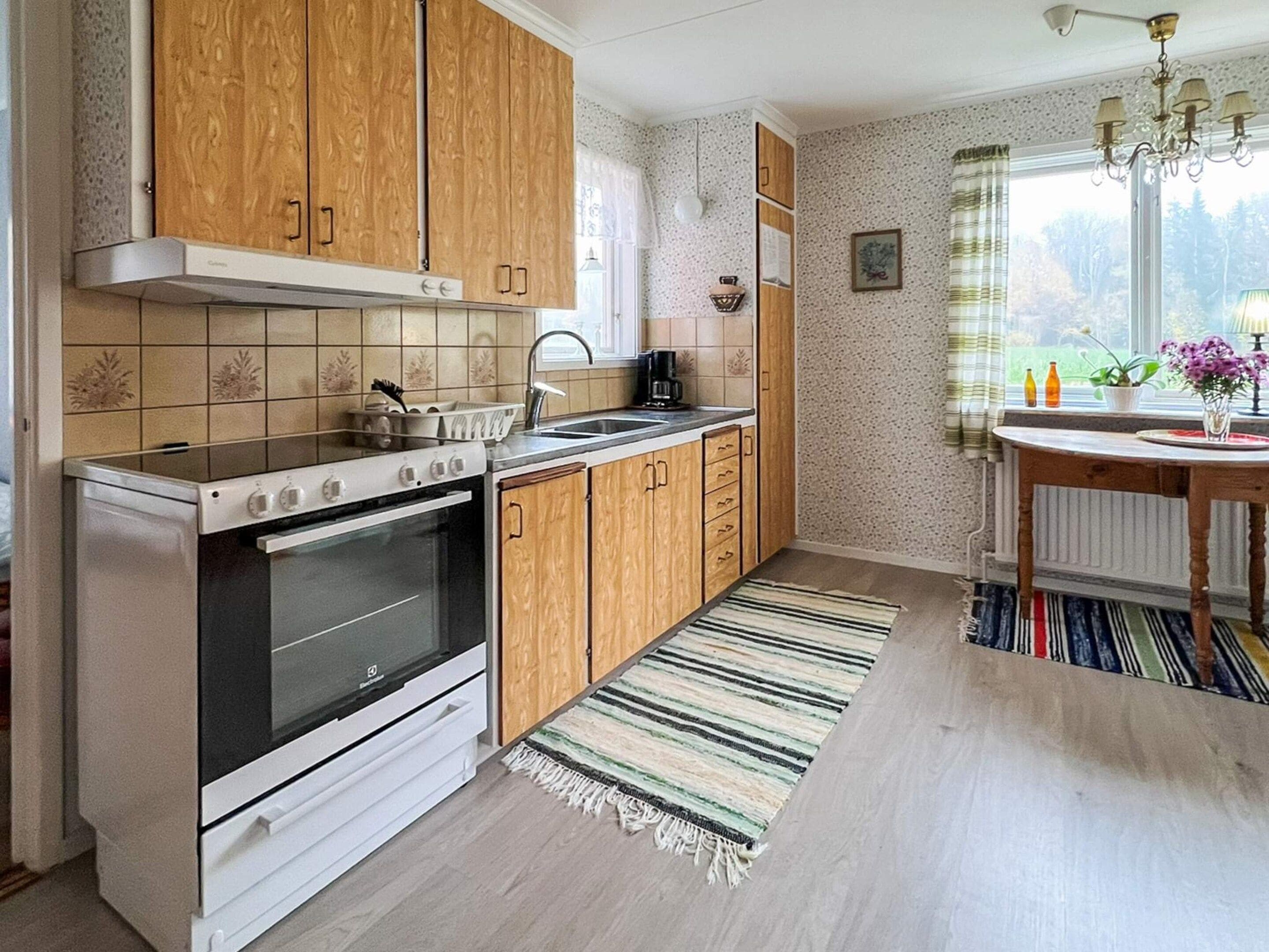 A kitchen with wooden cabinets, a stove, and a window with curtains.