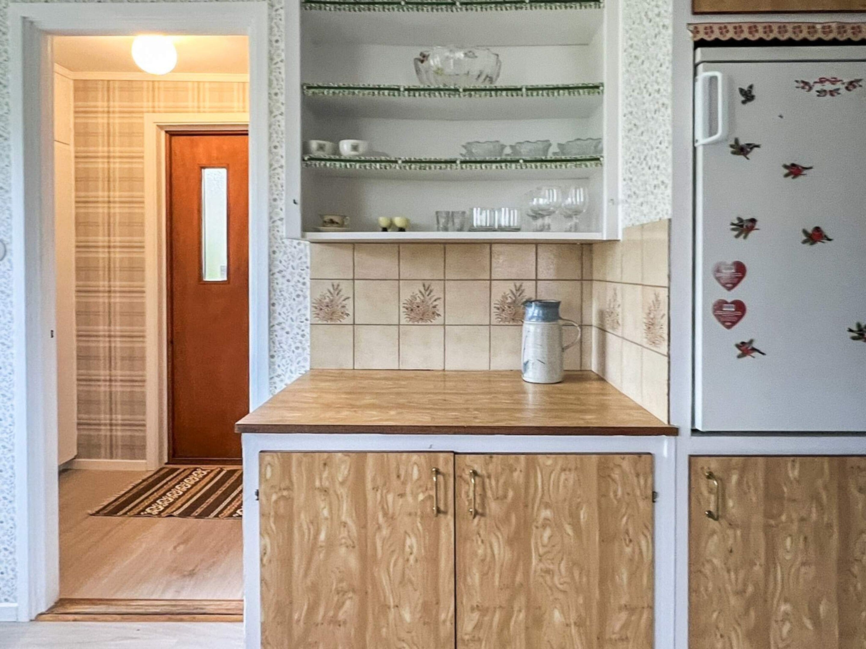 Una cocina con armarios de madera, un refrigerador blanco con imanes decorativos y salpicadero de azulejos.